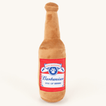 Tan plush beer-bottle dog toy with a red Barkweiser label reading Dog of Beers, on a plain cream background