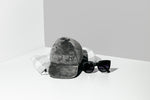 Grey plush Pawritzia cap dog toy styled with a plaid cloth and sunglasses on a grey studio backdrop